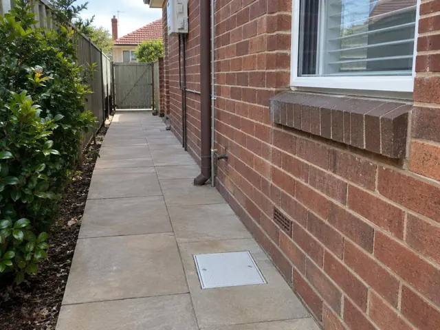 Outdoor tiled side path beside a brick house with a drain grate and clean paving in Hurstville