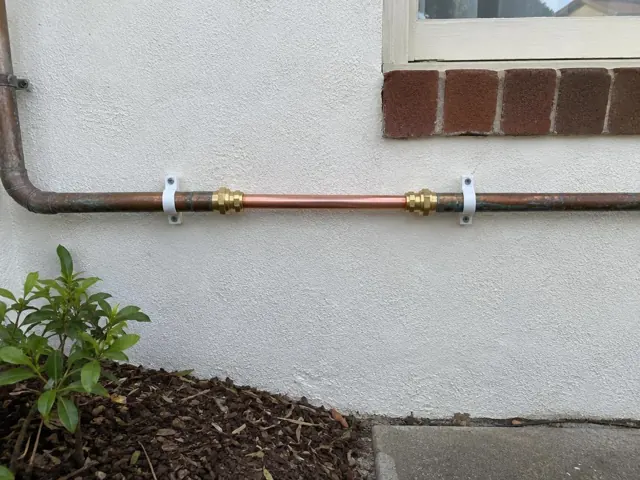 Exterior wall with a repaired copper water pipe section beneath a window in Rockdale