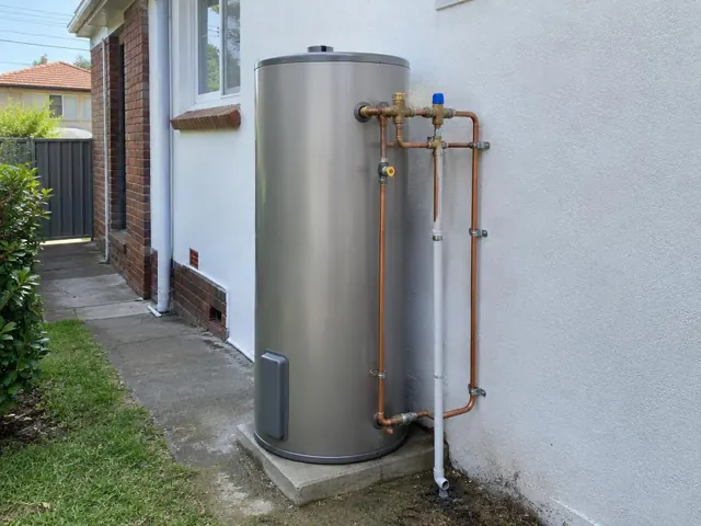 Outdoor hot water cylinder with copper pipework beside a house wall and narrow side path in Kogarah