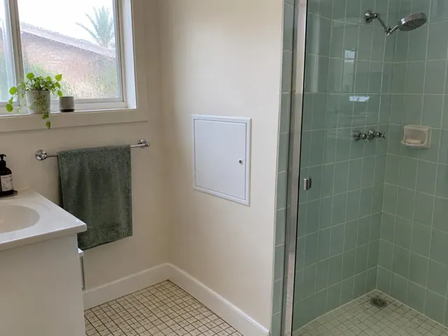 Bathroom wall with a small white access panel beside a tiled shower and vanity in Brighton-Le-Sands